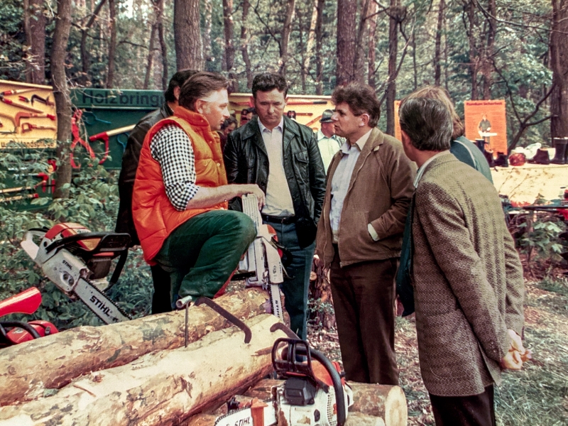 Eine Gruppe M&auml;nner im Wald, einer tr&auml;gt eine orangefarbene Weste