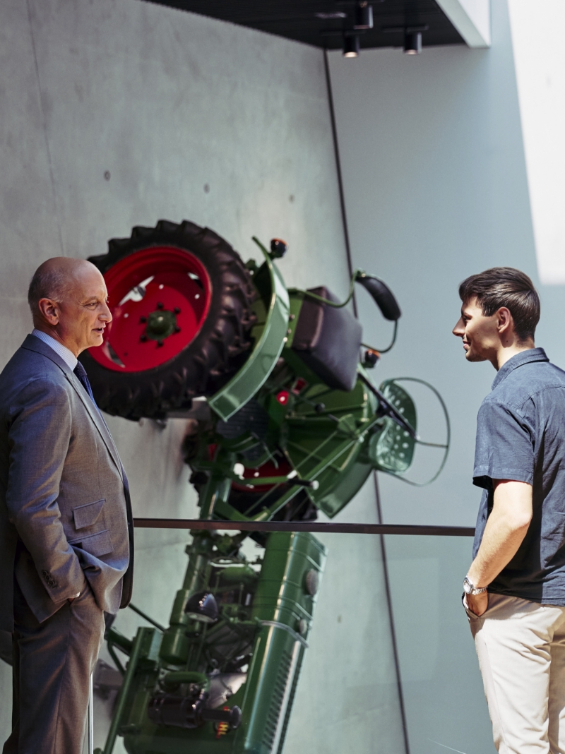 Dr. Nikolas Stihl und Tamino Soubawi im Gespr&auml;ch; im Hintergrund h&auml;ngt ein Traktor senkrecht an der Wand.