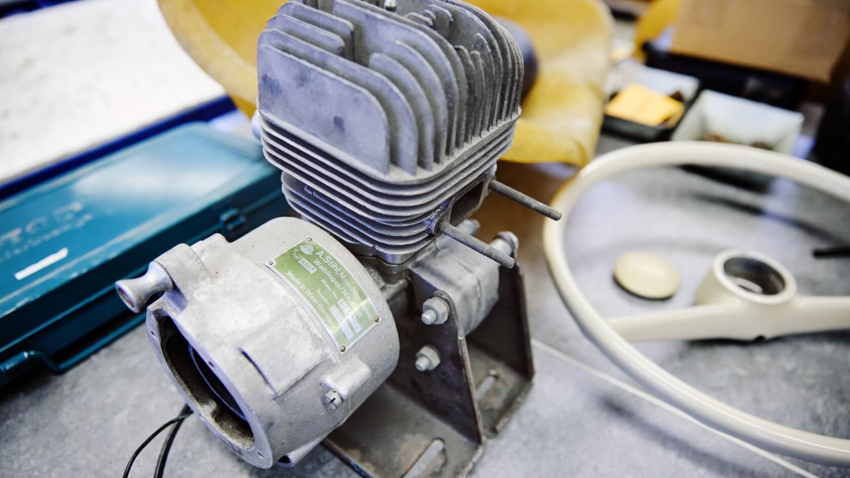 Nahaufnahme des demontierten Motors, daneben das Lenkrad und der Sitz des Gokarts.